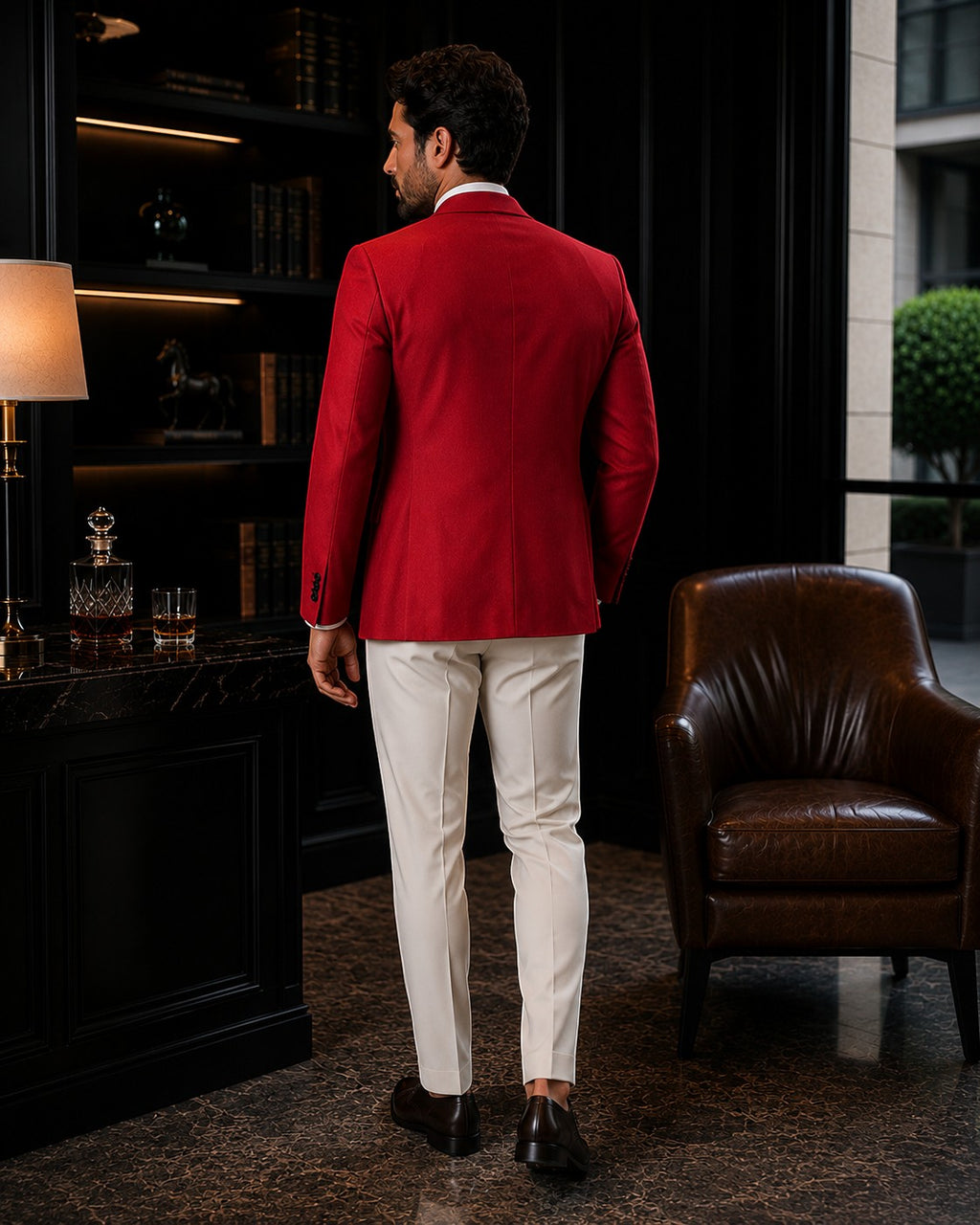 Man wearing a Barutti.ae red wool blazer with white trousers, viewed from the back in a luxury study.