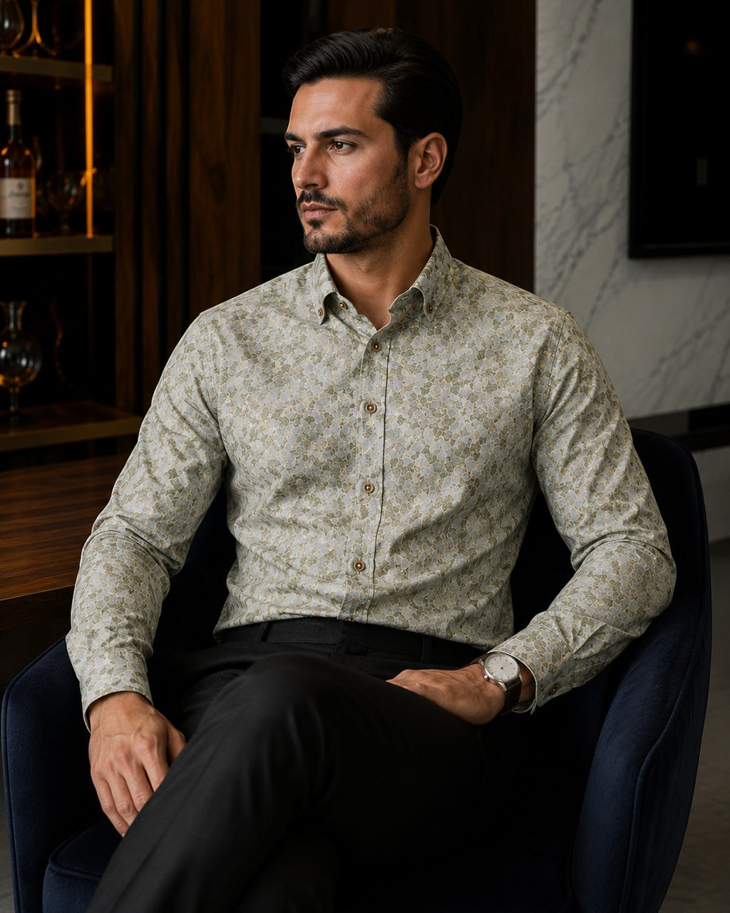 Barutti.ae Venti body-fit shirt in olive and sage leaf print with button-down collar, worn by a man in a dark chair.