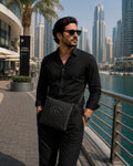 Man wearing a Barutti black leather crossbody bag with crocodile-embossed front in Dubai Marina.