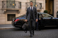 Man in a grey suit carrying a Barutti black leather Lucca weekender duffel bag.